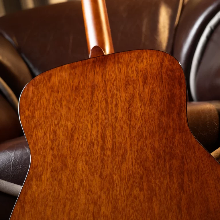 Close-up of an acoustic guitar back with a warm brown wood grain resting on a leather couch. ขายราคาพิเศษ