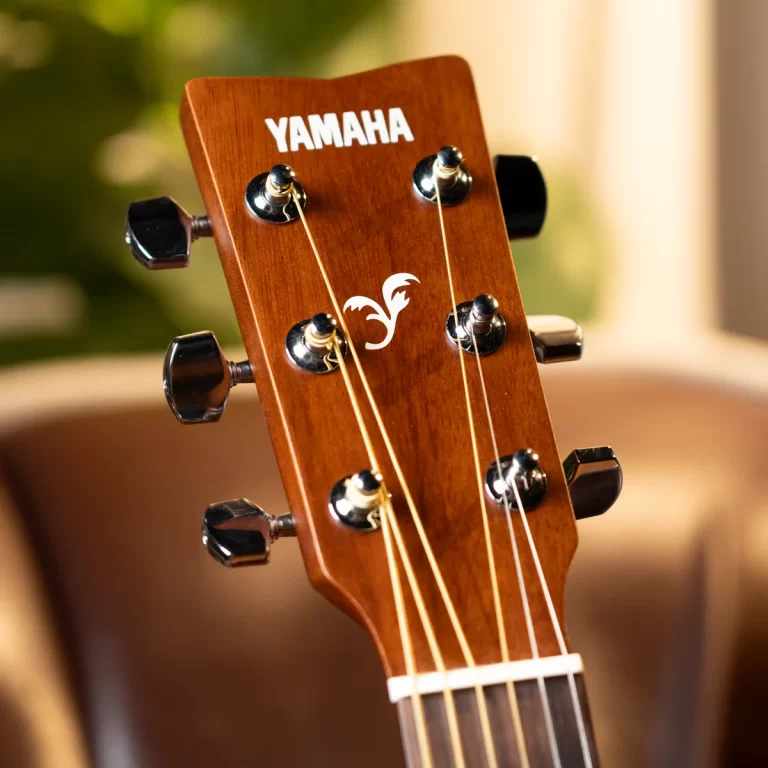 Close-up of a Yamaha acoustic guitar headstock showing six chrome tuners and light-colored strings on a warm wood finish, with the Yamaha logo visible at the top and a white nut at the bottom of the headstock. ขายราคาพิเศษ