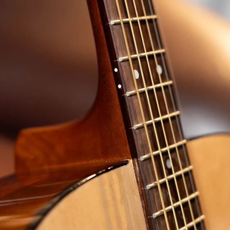 Close-up of an acoustic guitar neck showing frets, strings, and wood grain ขายราคาพิเศษ