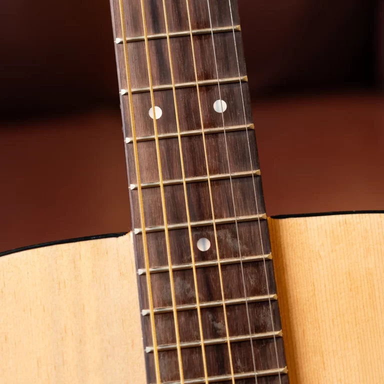 Close-up of an acoustic guitar neck showing frets, strings, and dot inlays on a wooden fretboard. ขายราคาพิเศษ
