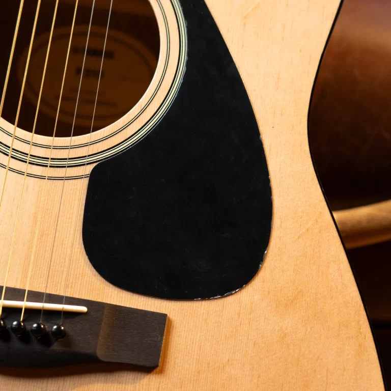 Close-up of an acoustic guitar's soundhole, strings, and black pickguard on a light wood body. ขายราคาพิเศษ
