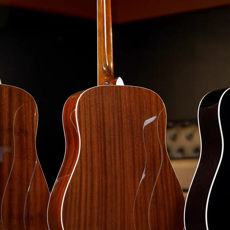 Close-up of three polished wooden acoustic guitar backs with warm brown finishes and curved bodies against a dark background. ขายราคาพิเศษ