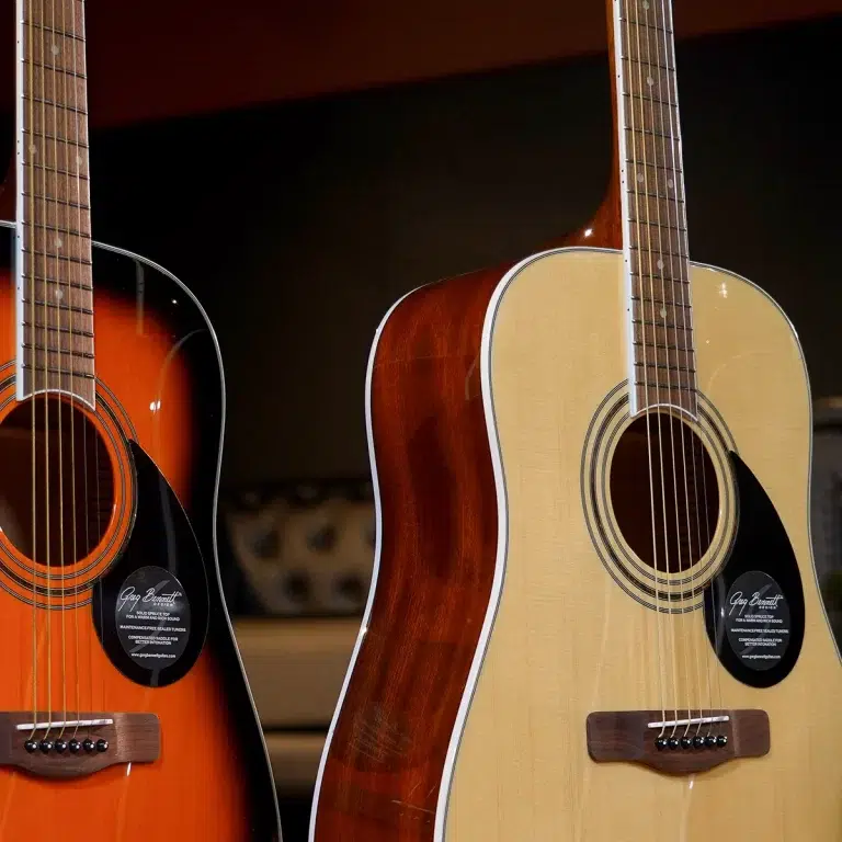 Two acoustic guitars standing side by side, one sunburst orange and one natural wood finish, showcasing soundholes and strings. ขายราคาพิเศษ