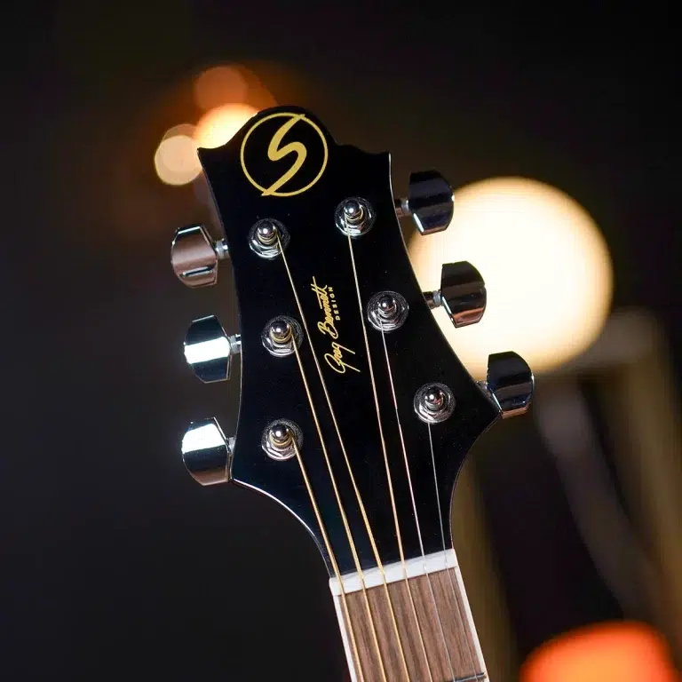 Close-up of a black guitar headstock with six chrome tuners, gold strings, and the Gibson logo in gold. ขายราคาพิเศษ