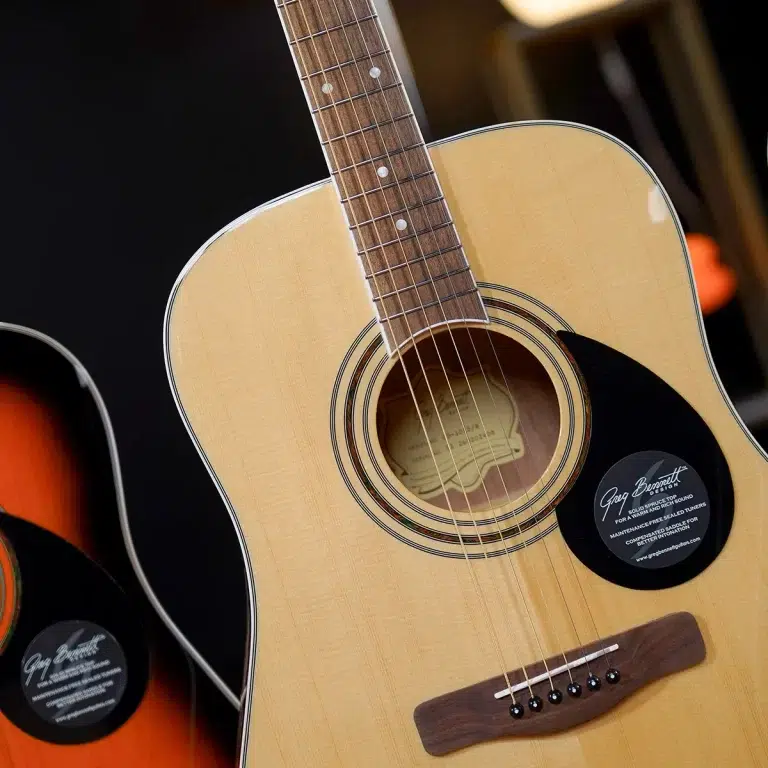 Close-up of an acoustic guitar showing its light wood body, soundhole with rosette, neck, and strings; a black circular badge is on the body near the soundhole. ขายราคาพิเศษ