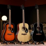 Three acoustic guitars on stands in a row: sunburst on the left, natural wood in the middle, black on the right, in a dim stage setting with warm lighting. ลดราคาพิเศษ