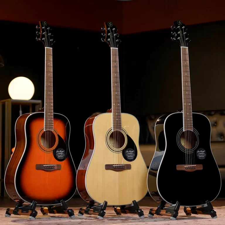 Three acoustic guitars on stands in a row: sunburst on the left, natural wood in the middle, black on the right, in a dim stage setting with warm lighting. ขายราคาพิเศษ