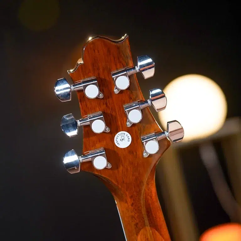 Close-up of a guitar headstock with six chrome tuning pegs on a warm wooden neck, blurred background lights ขายราคาพิเศษ