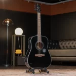 Black acoustic guitar on a stand in a stylish studio lounge with a tufted sofa and warm lighting in the background. ขายราคาพิเศษ