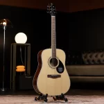 Acoustic guitar on a stand in a dim, stylish living room with a glowing floor lamp in the background. ขายราคาพิเศษ