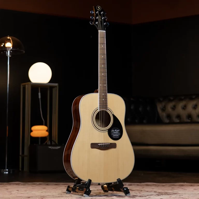 Acoustic guitar on a stand in a dim, stylish living room with a glowing floor lamp in the background. ขายราคาพิเศษ