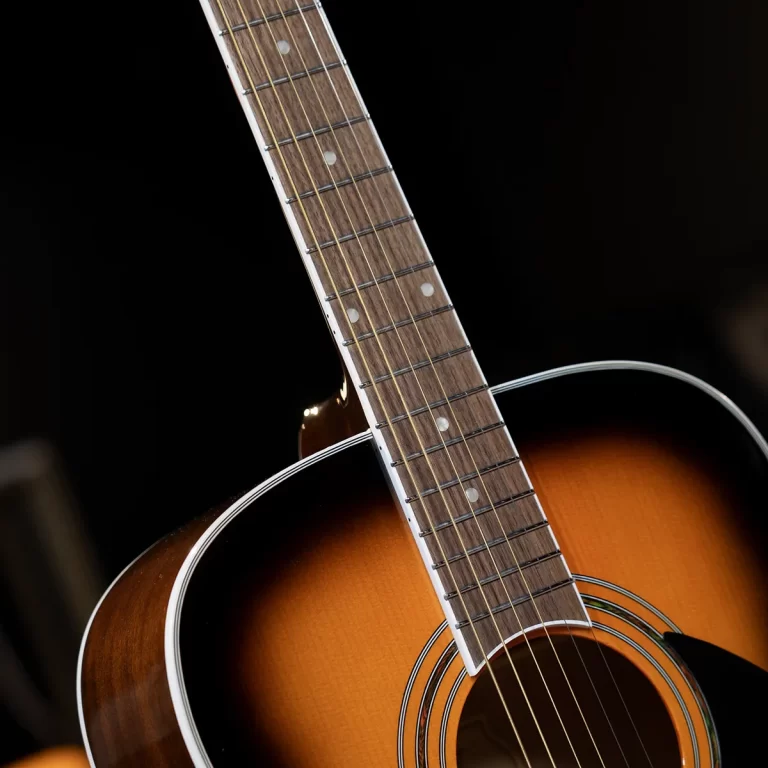 Close-up of a sunburst acoustic guitar neck and body, showing frets, fret markers, and six strings against a dark background ขายราคาพิเศษ