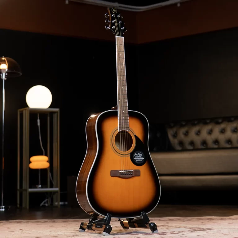 Sunburst acoustic guitar on a stand in a dim studio lounge with warm lighting and a tufted sofa in the background. ขายราคาพิเศษ
