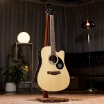 Cream-colored acoustic guitar on a wooden stand in a cozy showroom with a glowing globe lamp and plants in the background, soft lighting ลดราคาพิเศษ