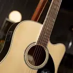 Close-up of a light wood acoustic guitar showing the body, soundhole, and the fretboard with strings and dots on the neck.