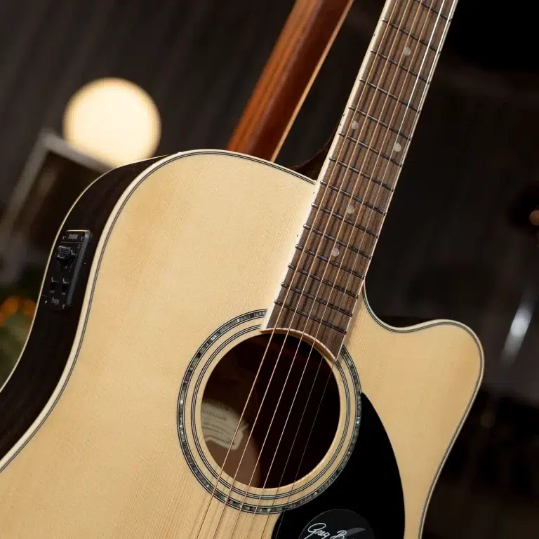 Close-up of a light wood acoustic guitar showing the body, soundhole, and the fretboard with strings and dots on the neck.