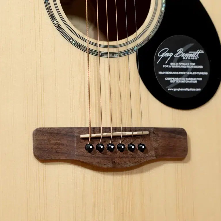 Close-up of an acoustic guitar showing the bridge with six strings and black bridge pins, plus a circular label on the body. ขายราคาพิเศษ
