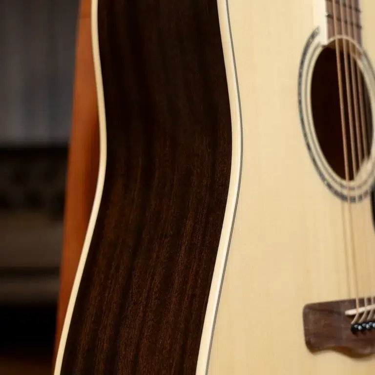 Close-up of an acoustic guitar showing the light top, dark back, and visible strings over the soundhole rim. ขายราคาพิเศษ