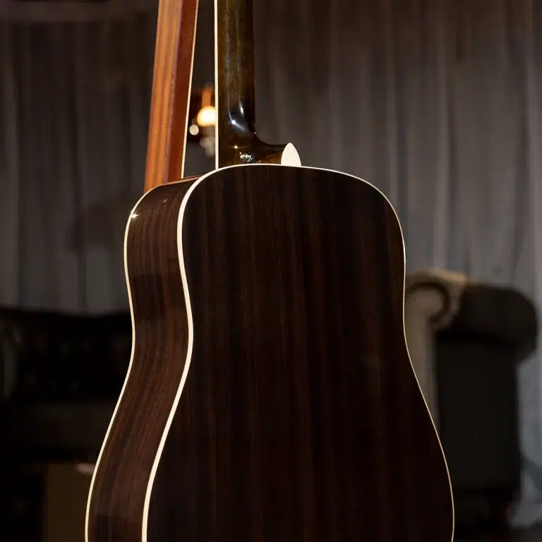 Back of a dark wood acoustic guitar with white binding, hanging in a dim room ขายราคาพิเศษ