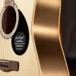 Close-up of an acoustic guitar body showing the soundhole, light wood top, and darker side with a rounded edge; a black circular pickguard sticker is visible near the strings. ขายราคาพิเศษ