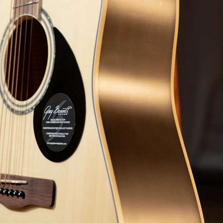 Close-up of an acoustic guitar body showing the soundhole, light wood top, and darker side with a rounded edge; a black circular pickguard sticker is visible near the strings. ขายราคาพิเศษ
