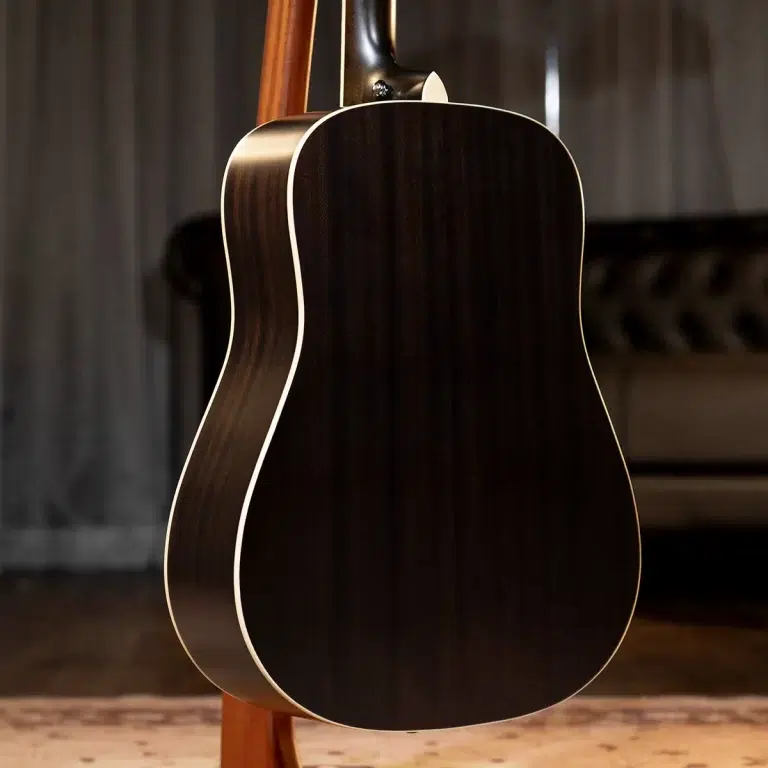 Back of a dark wood acoustic guitar with cream binding, resting on a stand. ขายราคาพิเศษ