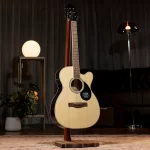 Acoustic guitar on a wooden stand in a softly lit studio room with a lamp in the background. ลดราคาพิเศษ