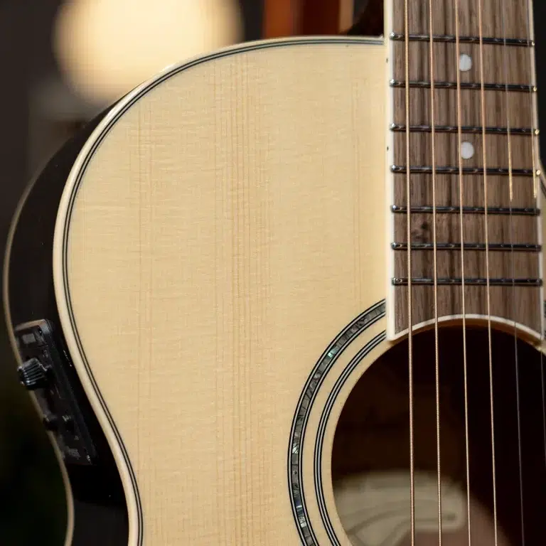 Close-up of an acoustic guitar's body and fretboard with strings visible across the neck, highlighting wood grain and rosette edge. ขายราคาพิเศษ
