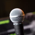 Close-up of a Shure SM58 vocal microphone with a metal mesh grille, angled against a dark background. ขายราคาพิเศษ