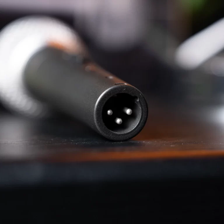 Close-up of a 3-pin circular audio connector end on a black cable resting on a wooden surface. ขายราคาพิเศษ
