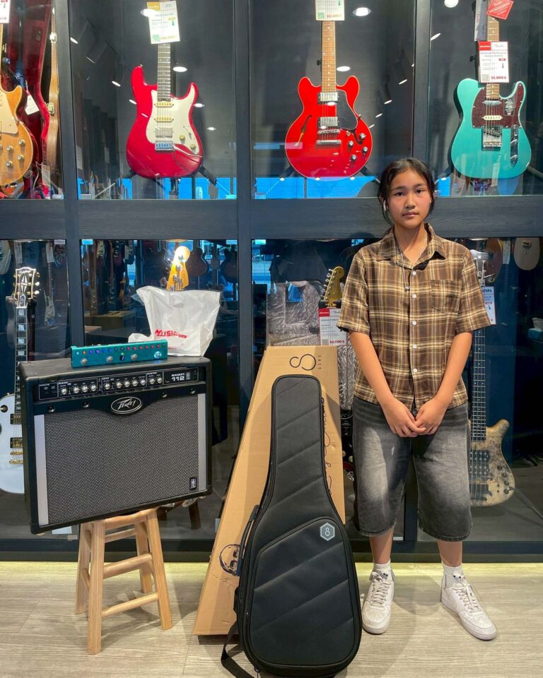 Girl in a plaid shirt stands beside a display of electric guitars in a music shop.