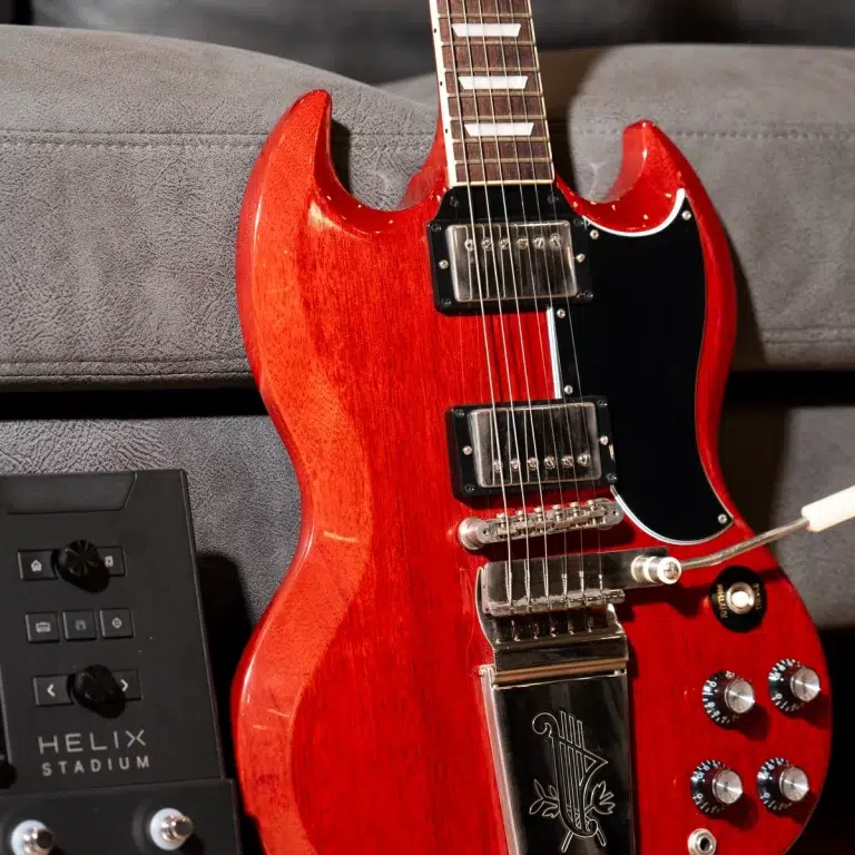 Red electric guitar with black pickguard and chrome hardware resting on a gray sofa, showing two humbucker pickups and knob controls nearby. ขายราคาพิเศษ