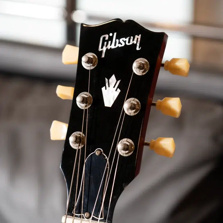Close-up of a black Gibson guitar headstock with six cream tuning pegs and strings visible by the logo: Gibson ขายราคาพิเศษ