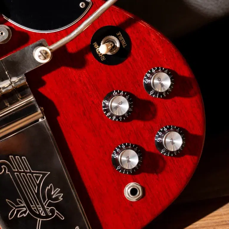 Close-up of a red electric guitar body showing four metal knob controls labeled Volume and Tone, with a chrome bridge and black pickguard edge visible. ขายราคาพิเศษ