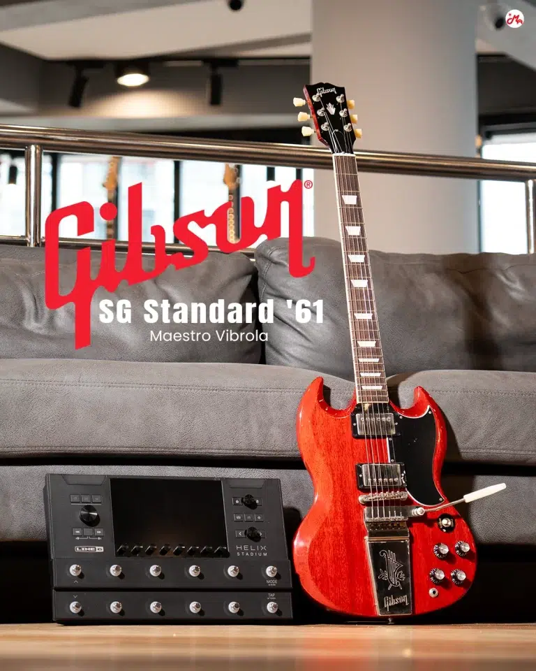 Gibson SG Standard ’61 Maestro Vibrola guitar in red, resting against a gray couch with a Line 6 unit nearby (text overlay reads ‘Gibson SG Standard ’61 Maestro Vibrola'). ขายราคาพิเศษ