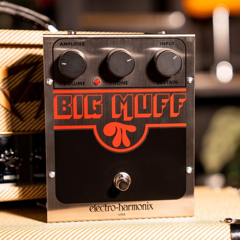 Electro-Harmonix Big Muff guitar effects pedal with three knobs (Volume, Tone, Sustain) on a brushed metal face and a red logo, footswitch at the bottom on a textured surface. ขายราคาพิเศษ