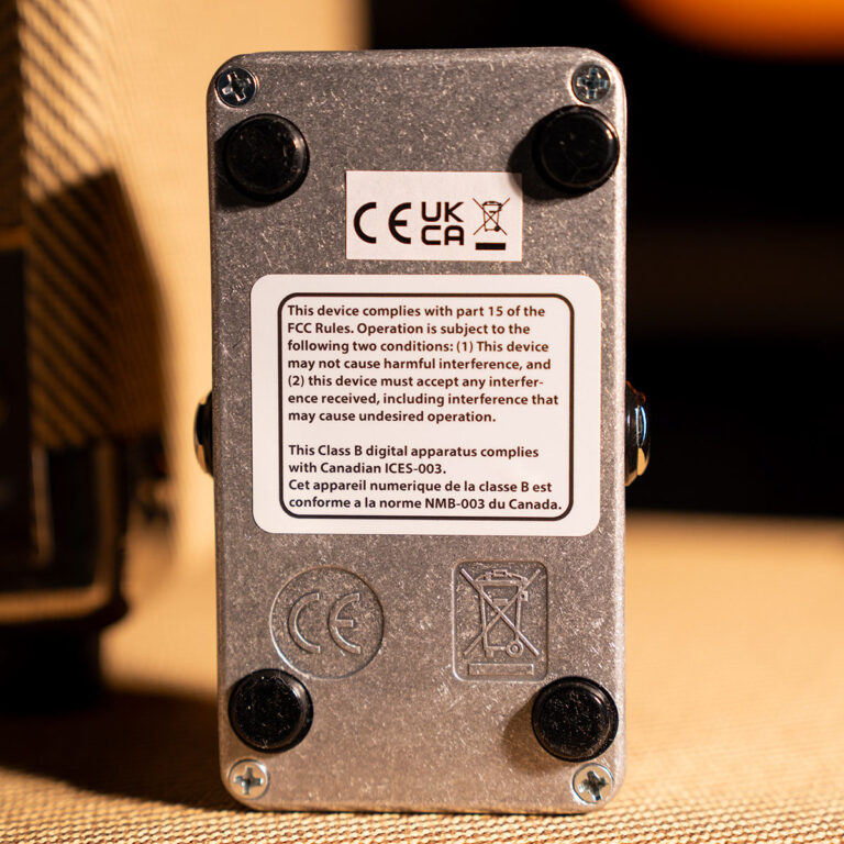 Back panel of a metal electronic device showing a CE/UKCA compliance sticker and a bilingual safety warning label containing FCC interference information. ขายราคาพิเศษ
