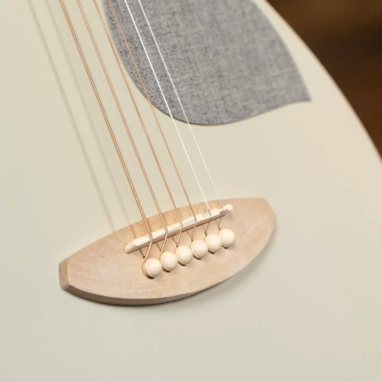 Close-up of an acoustic guitar bridge with six strings and white bridge pins on a pale wooden saddle edges the image. ขายราคาพิเศษ
