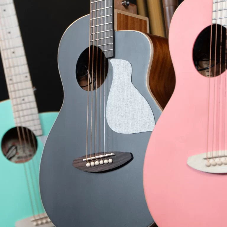 Close-up of several colorful acoustic guitars standing together: a blue-gray guitar in the center with a white pickguard, a pink guitar to the right, and a turquoise guitar to the left. ขายราคาพิเศษ
