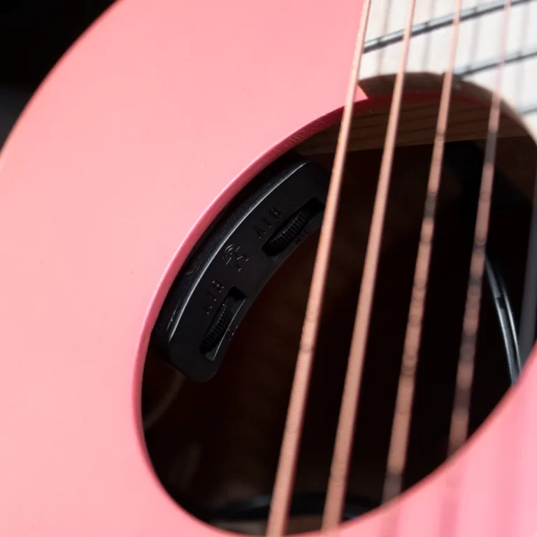 Close-up of a pink acoustic guitar soundhole with a black pickup control inside and copper strings in the foreground. ขายราคาพิเศษ