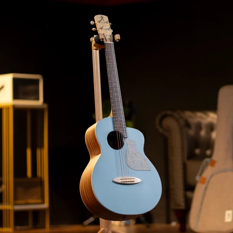 Blue acoustic guitar on a stand in a dim workshop, with blurred background objects nearby ขายราคาพิเศษ
