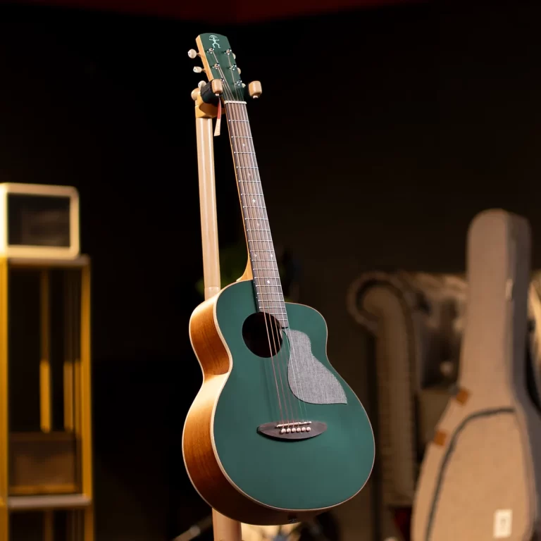 Green acoustic guitar on a stand in a dimly lit music room with cases in the background batter. ขายราคาพิเศษ