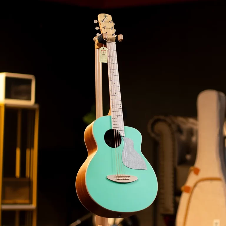 Teal acoustic guitar on a wooden stand in a dim room, with a gray pickguard and light-colored neck plates visible. ขายราคาพิเศษ