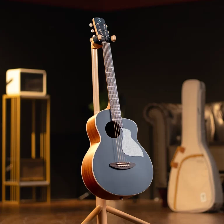 Blue-gray acoustic guitar on a wooden stand in a dim music studio, with blurred gear in the background. ขายราคาพิเศษ