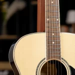 Close-up of an acoustic guitar showing a light wood top, dark fretboard, and metal strings across the neck. ขายราคาพิเศษ