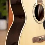 Close-up of an acoustic guitar showing the light wood body, dark pickguard edge, and soundhole with strings nearby. ขายราคาพิเศษ