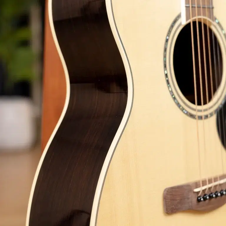 Close-up of an acoustic guitar showing the light wood body, dark pickguard edge, and soundhole with strings nearby. ขายราคาพิเศษ