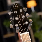 Close-up of a black guitar headstock with six chrome tuning pegs and a gold logo, strings wound around the pegs. (informative) ขายราคาพิเศษ