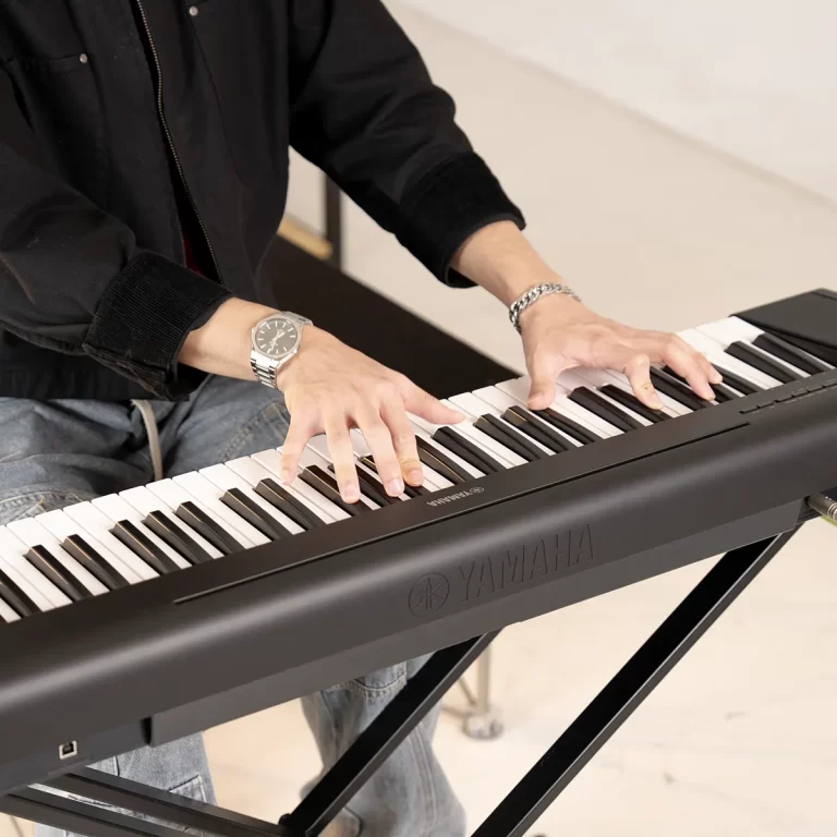Hands playing a Yamaha digital piano; the player wears a silver wristwatch and bracelet in a black jacket. ขายราคาพิเศษ