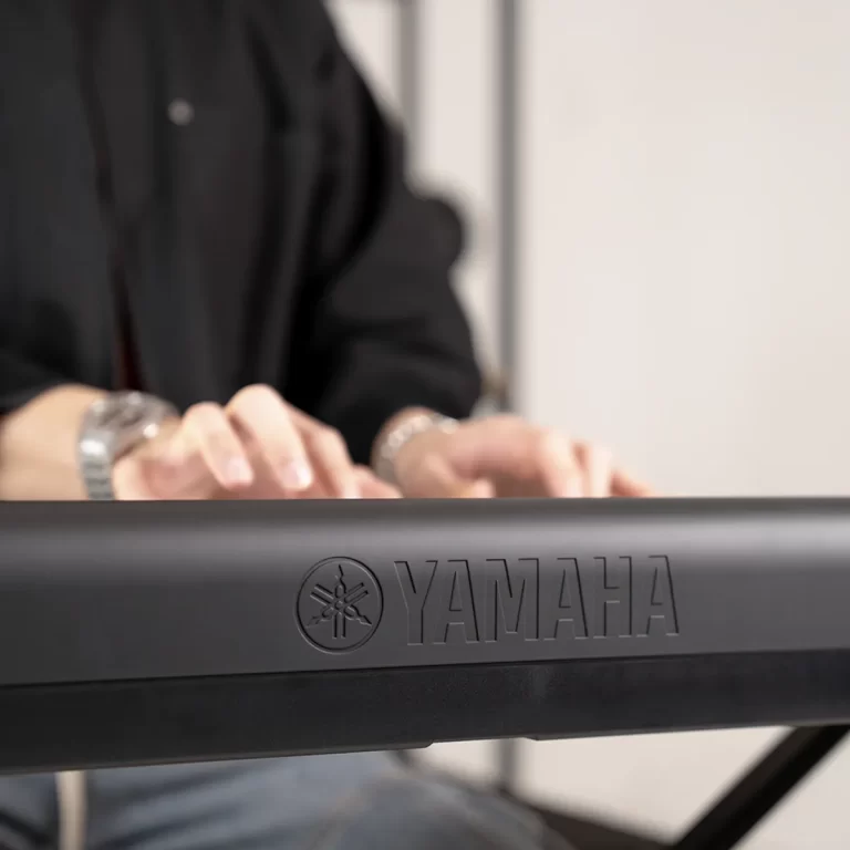Close-up of a person in a black shirt playing a Yamaha keyboard, hands on the keys with the Yamaha logo visible on the front edge ขายราคาพิเศษ